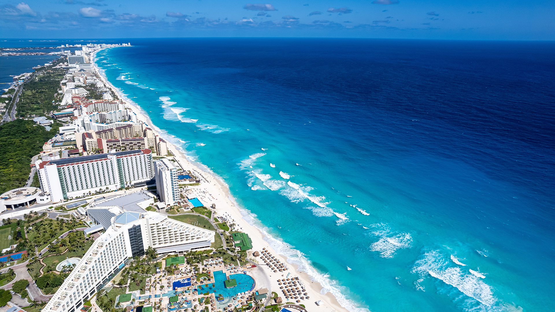 Aerial view of Cancún with modern beachfront hotels and bright turquoise waters under the Caribbean sun.