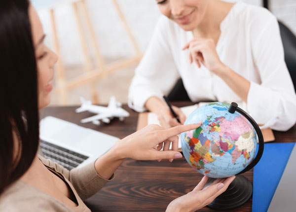 Sur un globe terrestre, une agente de voyage pointe un pays à sa cliente.
