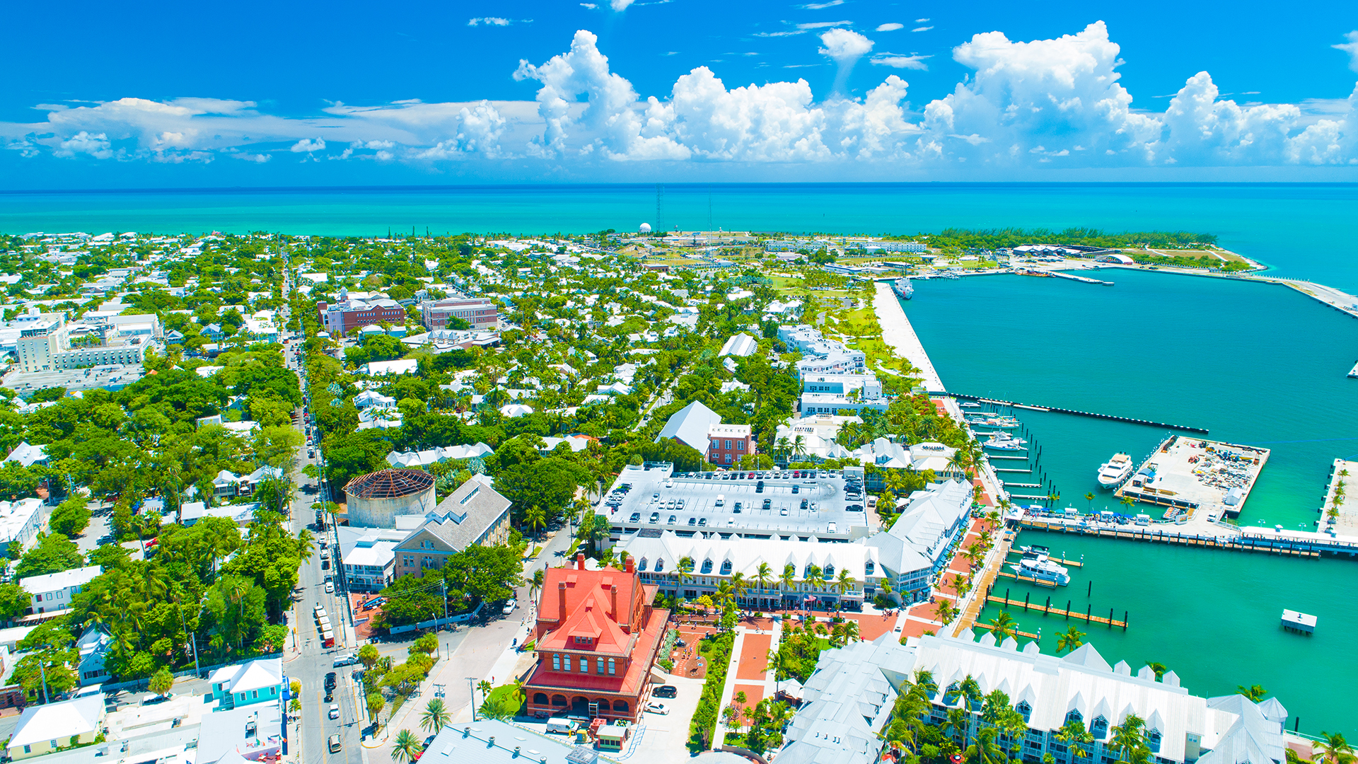 Aerial view of Key West, Florida, with colourful houses, tropical vegetation, and turquoise harbour waters under a blue sky.