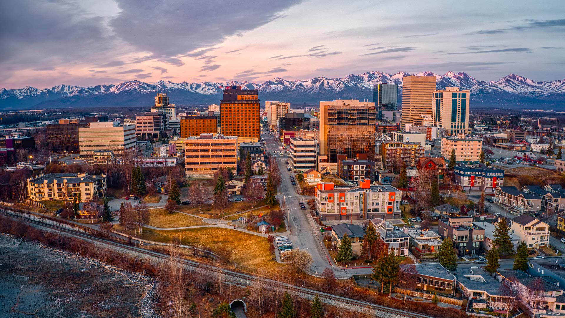 Vue aérienne de la ville d’Anchorage, en Alaska, avec ses bâtiments modernes et des montagnes enneigées en arrière-plan.