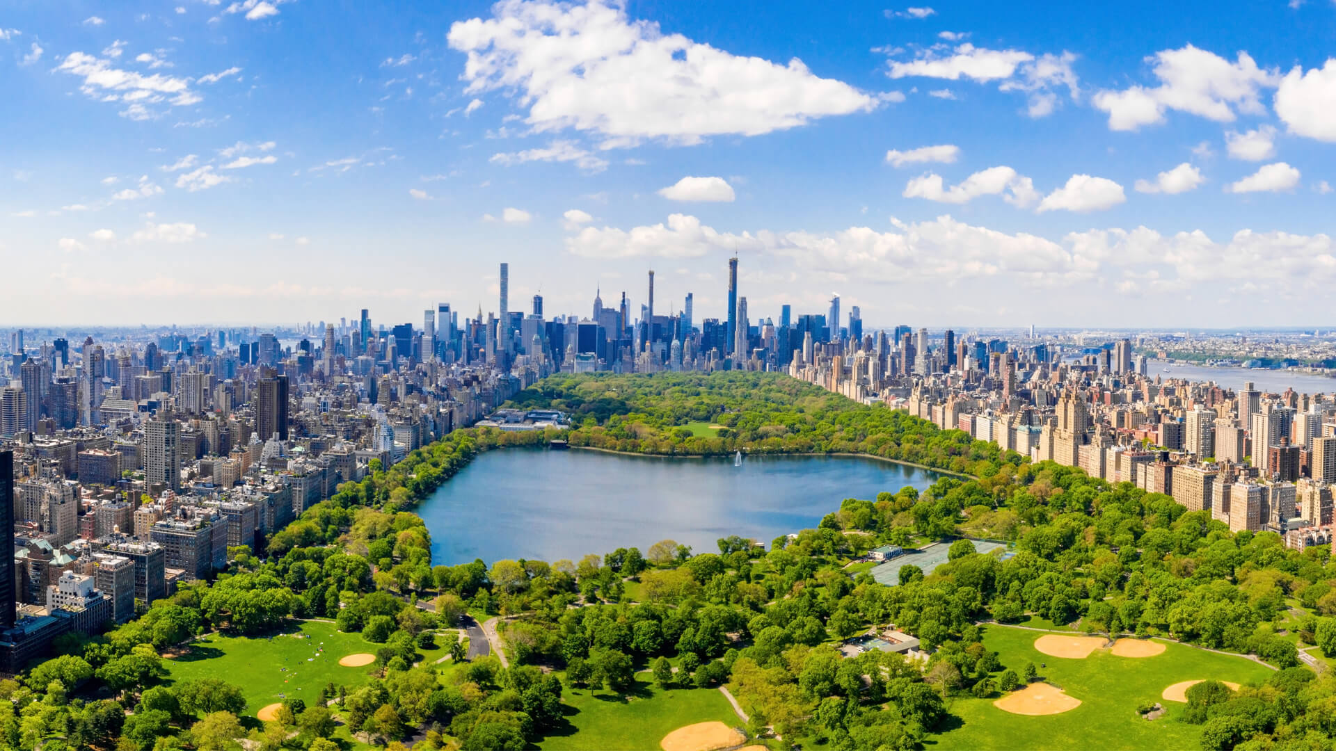 Vue aérienne de Central Park à New York, avec le lac, la végétation verdoyante, les gratte-ciel de Manhattan et le ciel bleu.