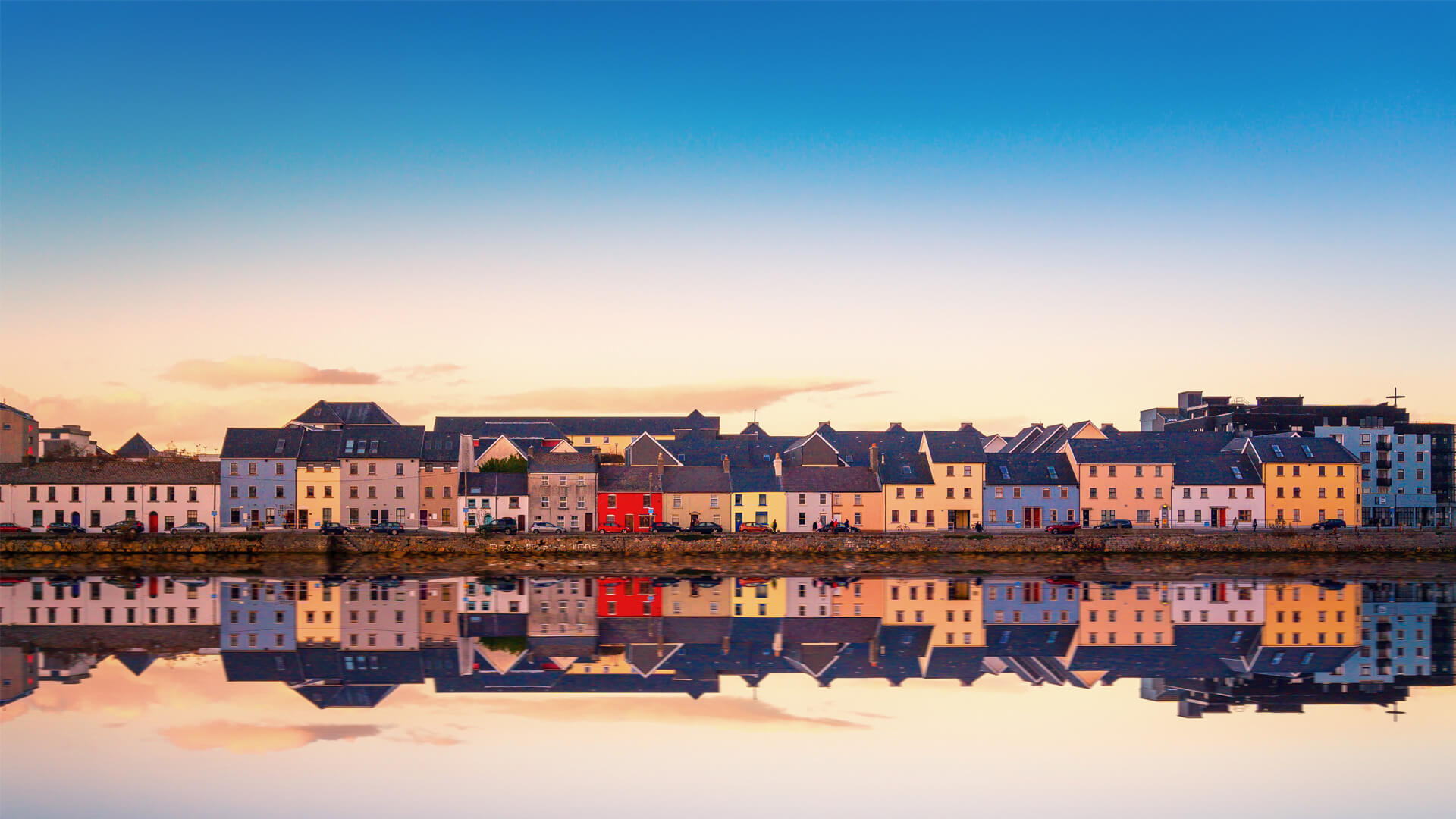 Colourful houses in Galway, Ireland, lined along the water and perfectly reflected under a soft pastel sky.