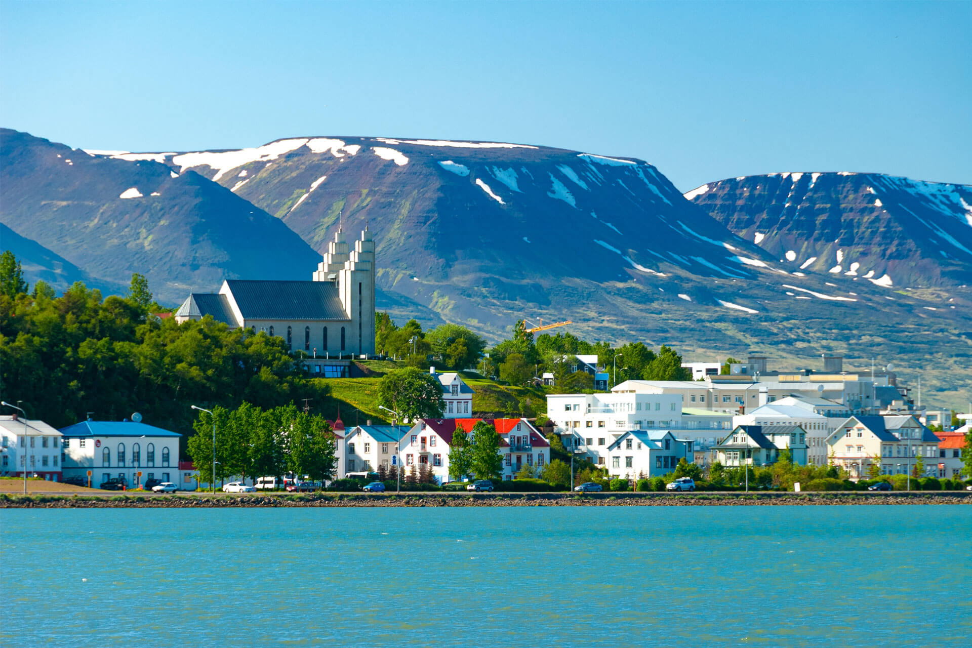 Picturesque view of Akureyri, Iceland, with Akureyrarkirkja church overlooking the town and snow-covered mountains in the background.