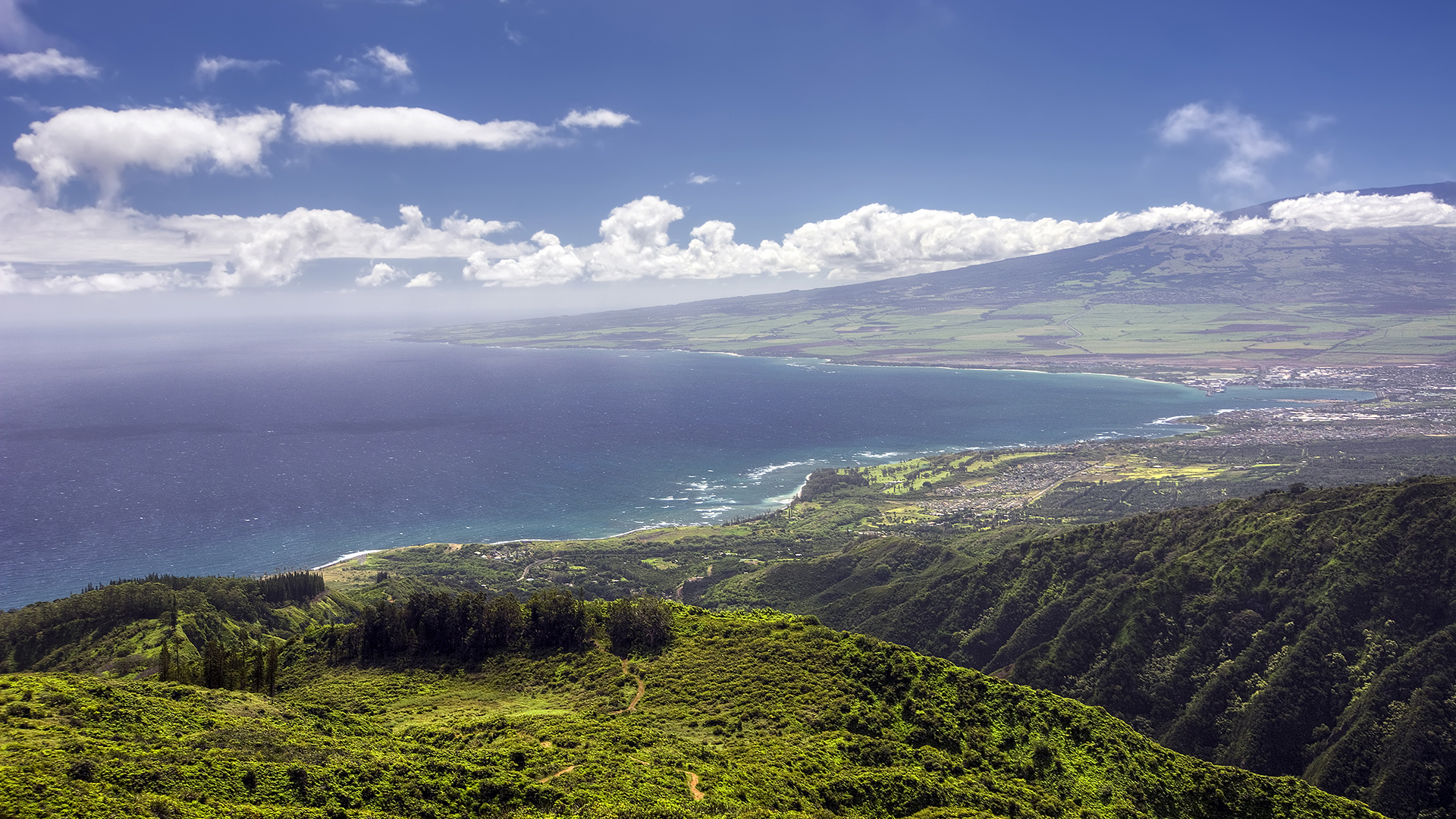 Vue aérienne de Kahului, à Hawaï, montrant l’océan Pacifique, les montagnes luxuriantes et les vastes pentes du Haleakalā en arrière-plan. 