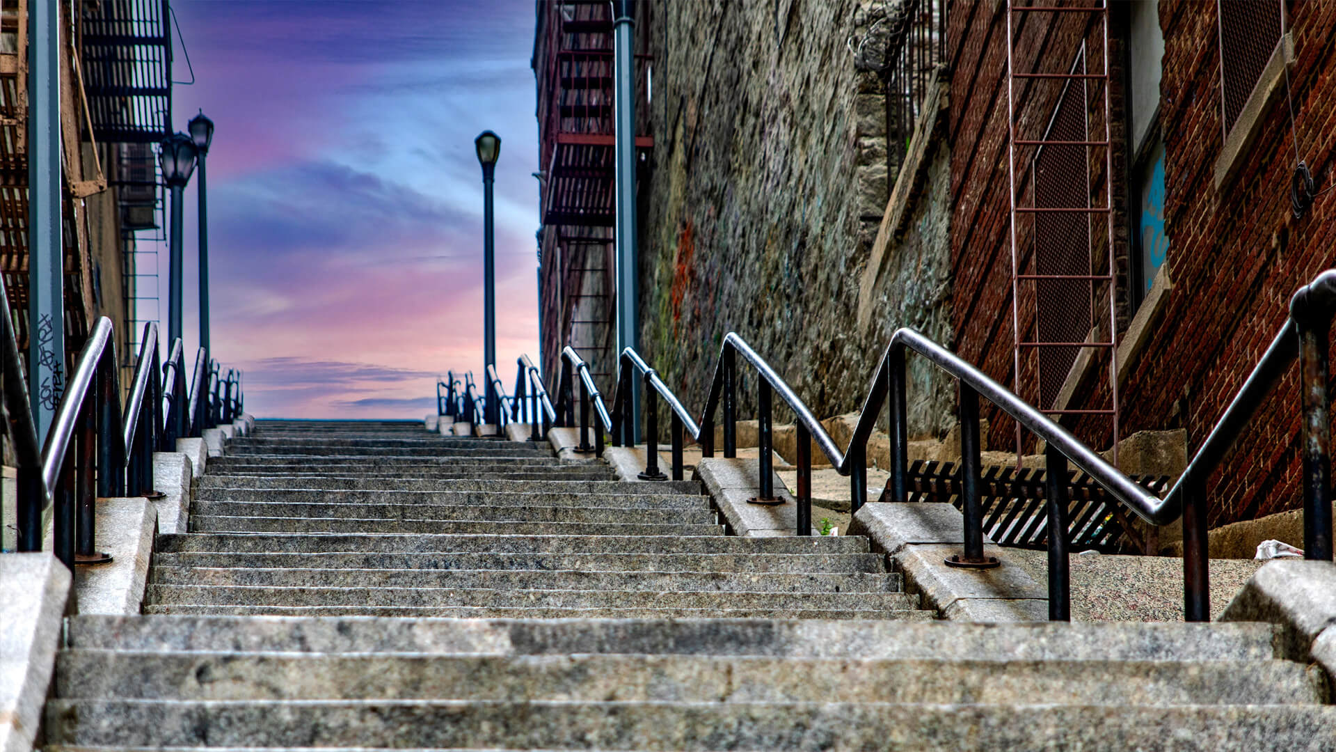 Iconic stone staircase in the Bronx, New York, at sunset, flanked by brick walls and metal railings.
