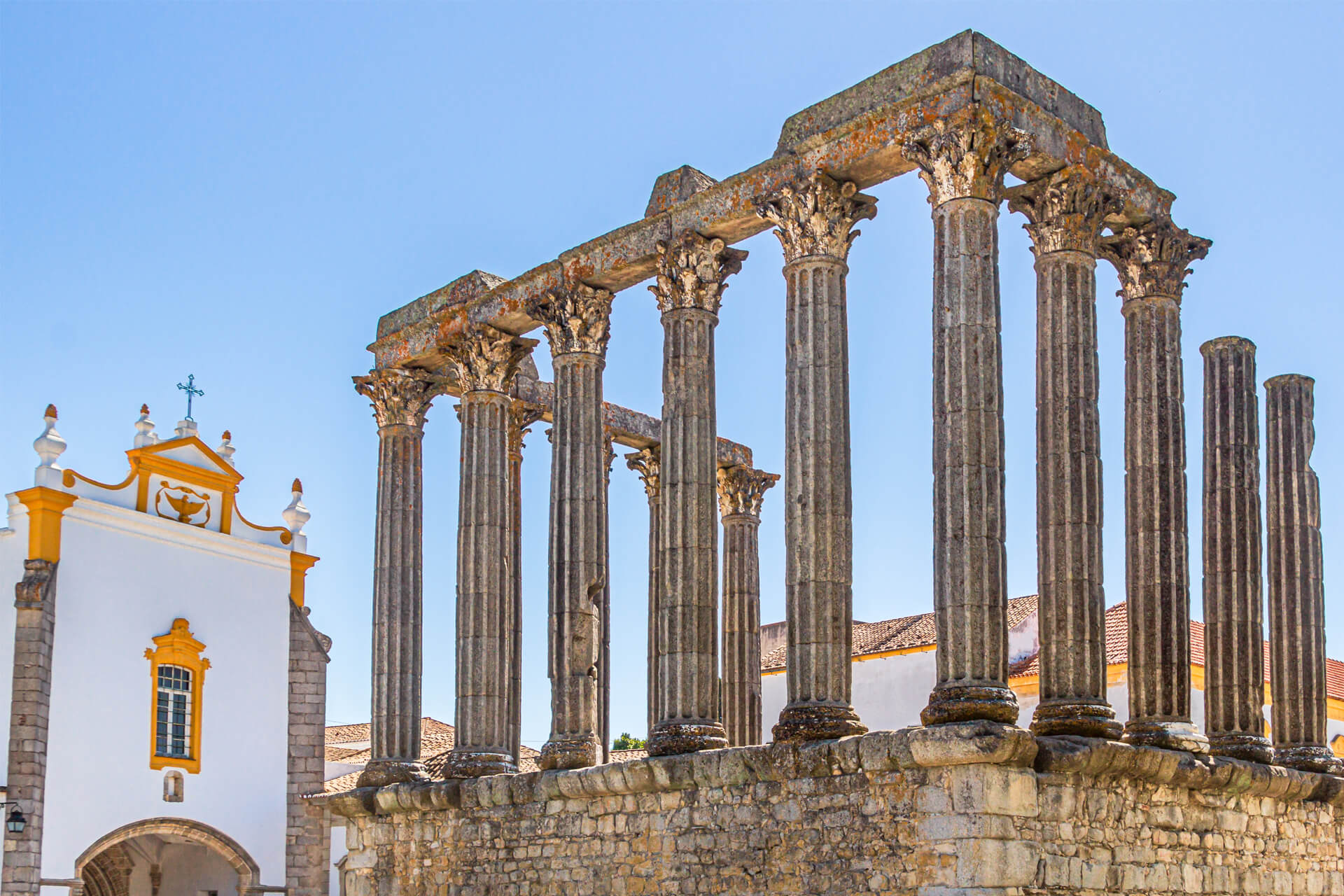 Roman Temple of Évora, Portugal, featuring well-preserved Corinthian columns beside a white and yellow church.