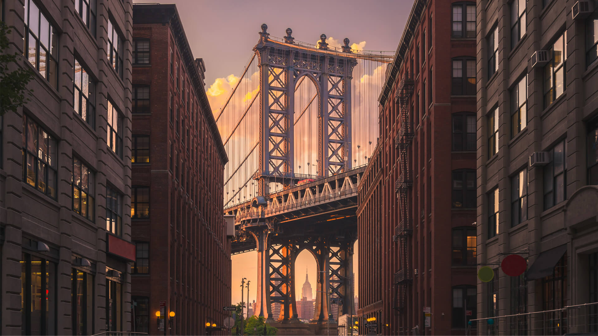Manhattan Bridge viewed from Brooklyn at sunset, with the Empire State Building framed by the bridge’s arch, in New York.