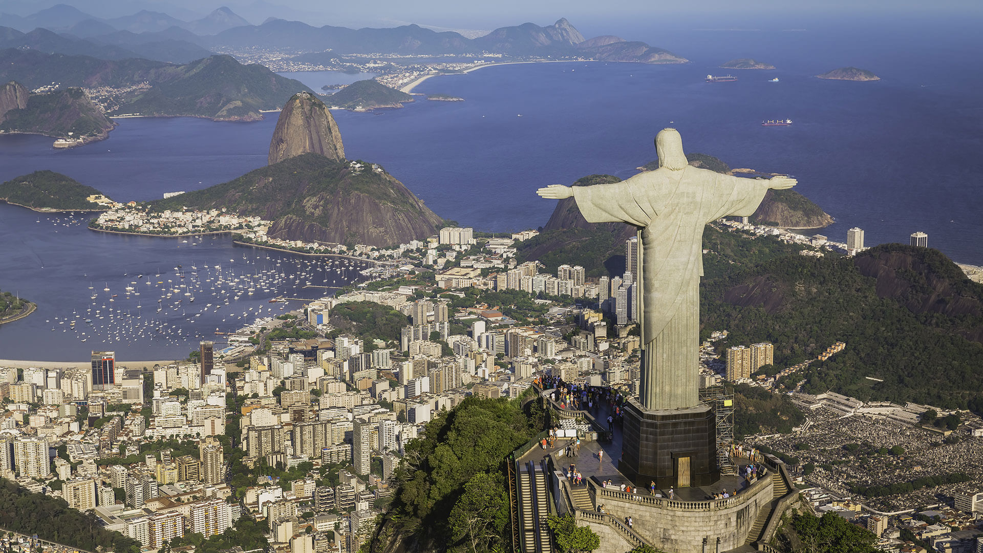 Aerial view of the massive Christ the Redeemer statue overlooking Rio de Janeiro, Guanabara Bay, and surrounding mountains.