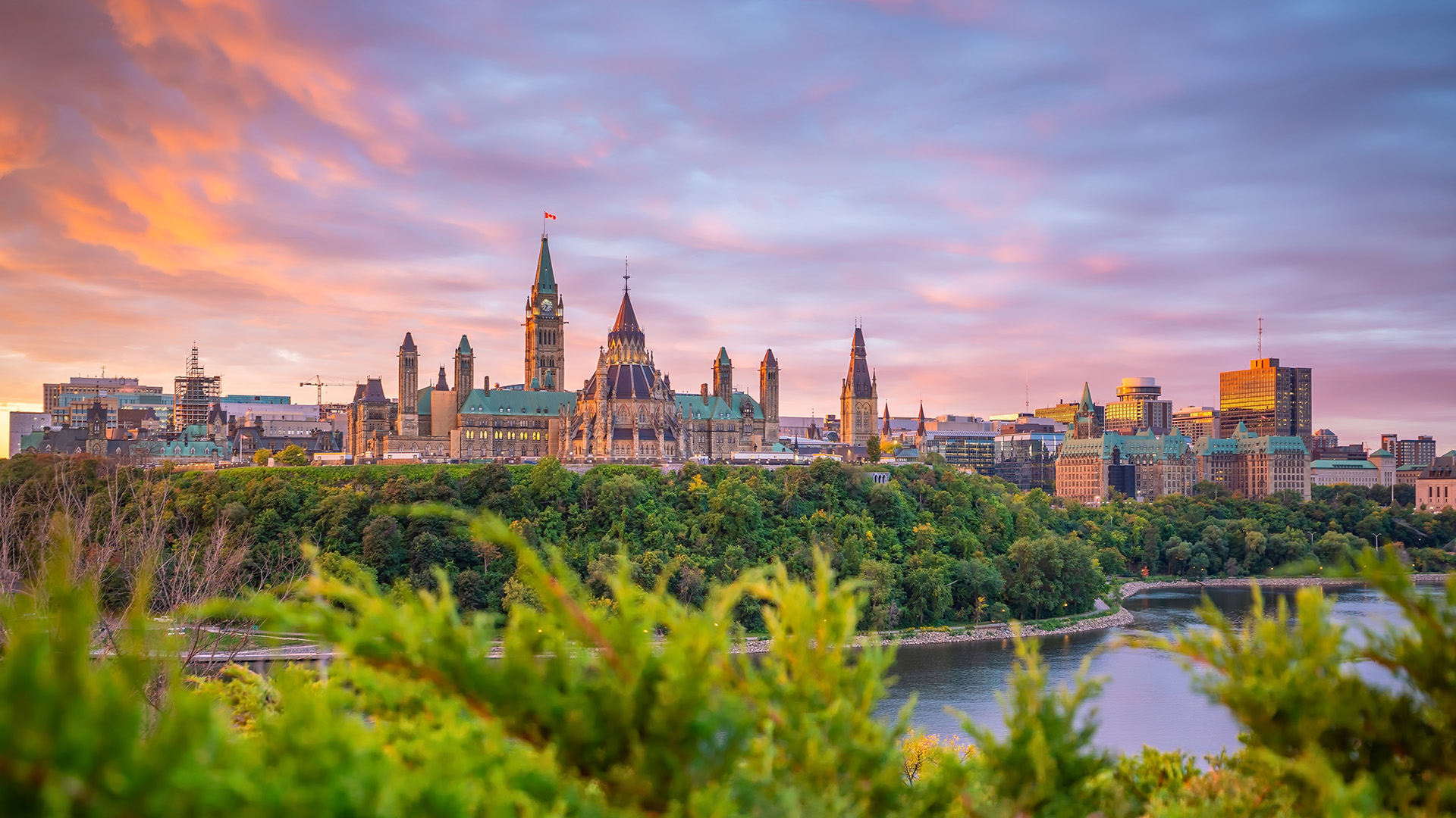Panoramic view of Ottawa and the Ottawa River at sunset, with Parliament Hill overlooking the city.