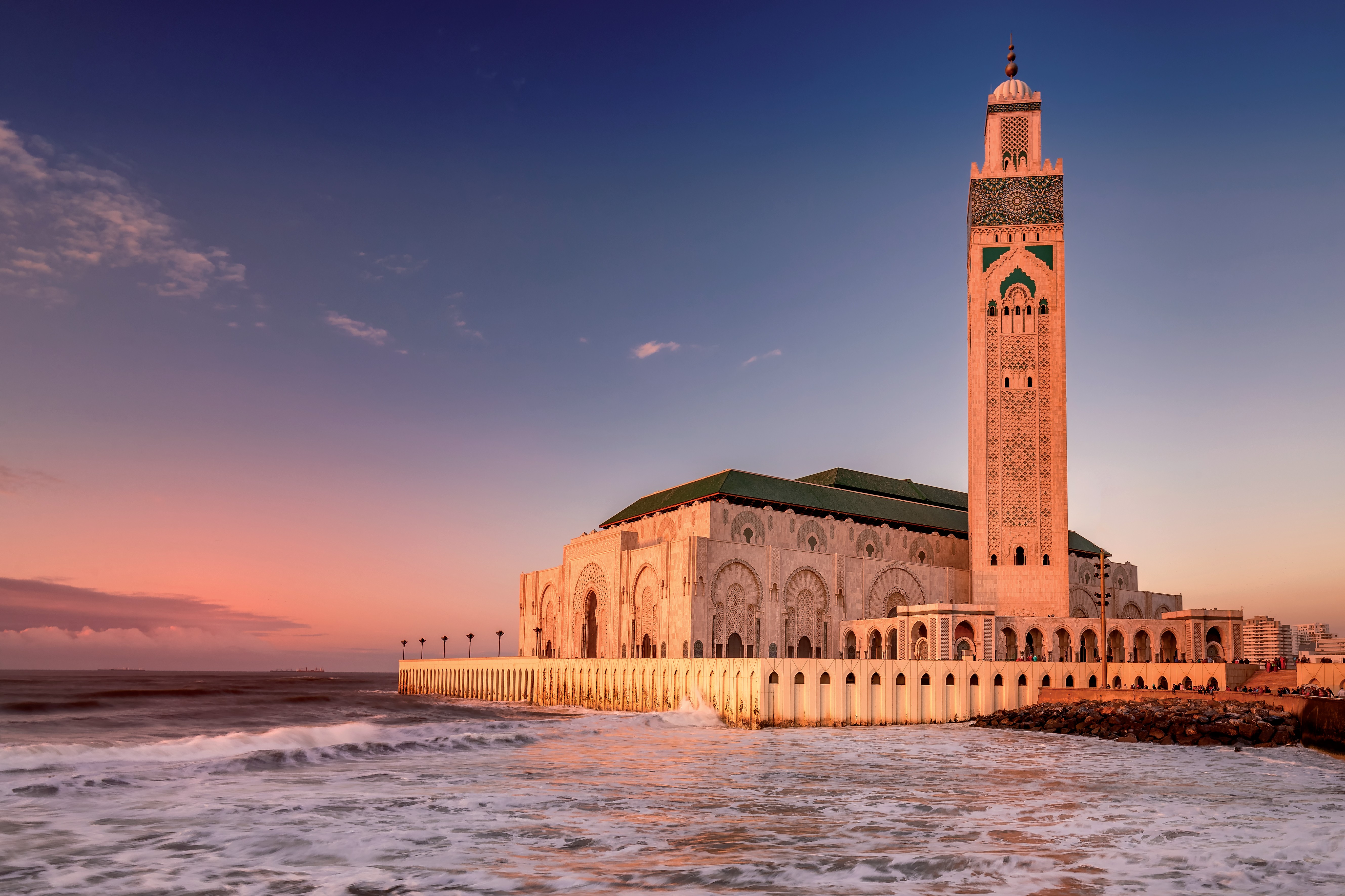 Hassan II Mosque in Casablanca, Morocco, at sunset, overlooking the Atlantic Ocean with gentle waves.