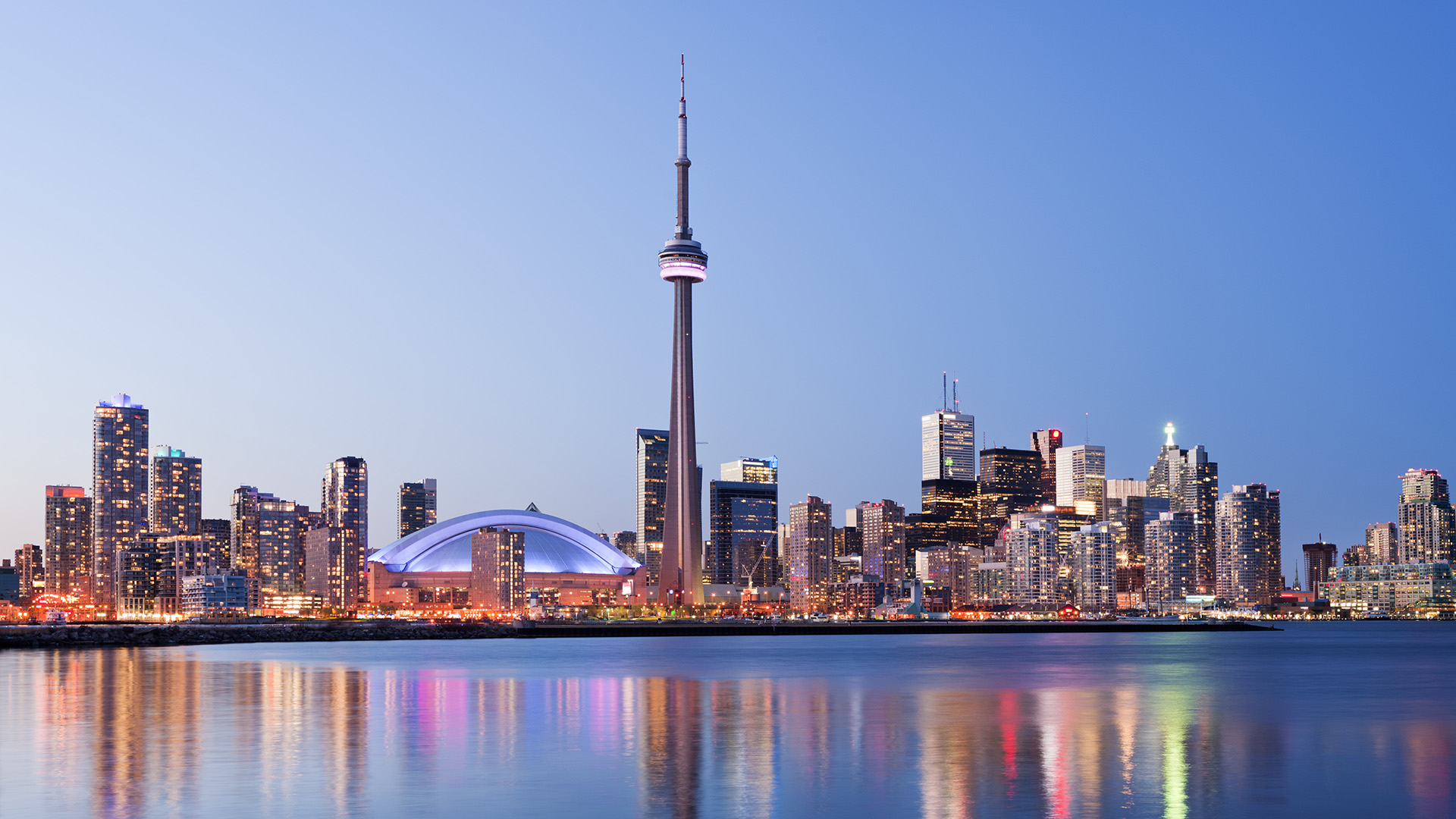 View of Toronto at dusk with the CN Tower and downtown city lights reflected on Lake Ontario, Canada.