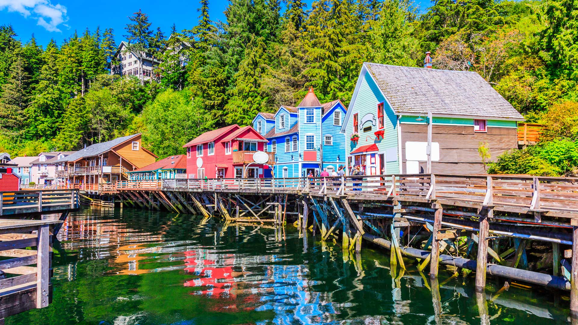 Maisons colorées sur pilotis le long de Creek Street à Ketchikan, au bord d’une eau calme et entourées de forêt en Alaska.