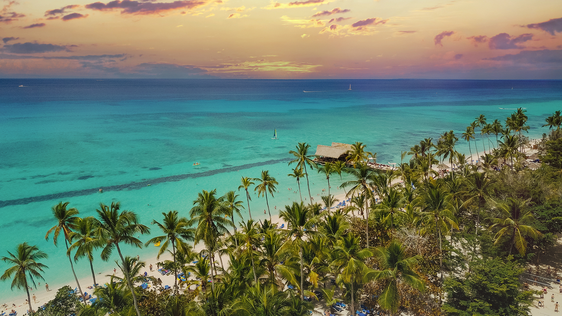Aerial view of a La Romana tropical beach at sunset, with palm trees and turquoise waters.