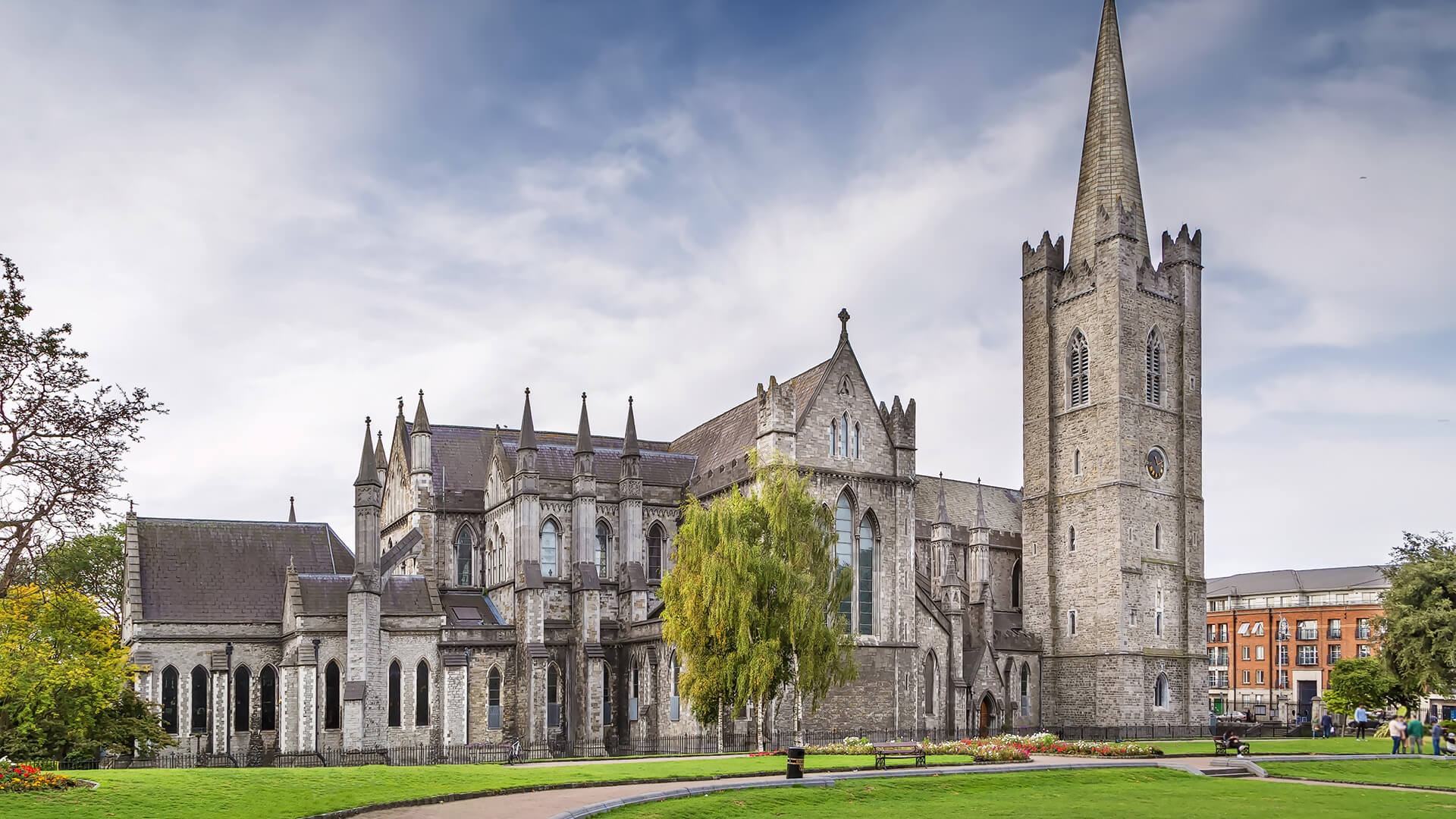 Gothic-style St. Patrick’s Cathedral in grey stone, surrounded by lush green lawns under a bright sky, Dublin.