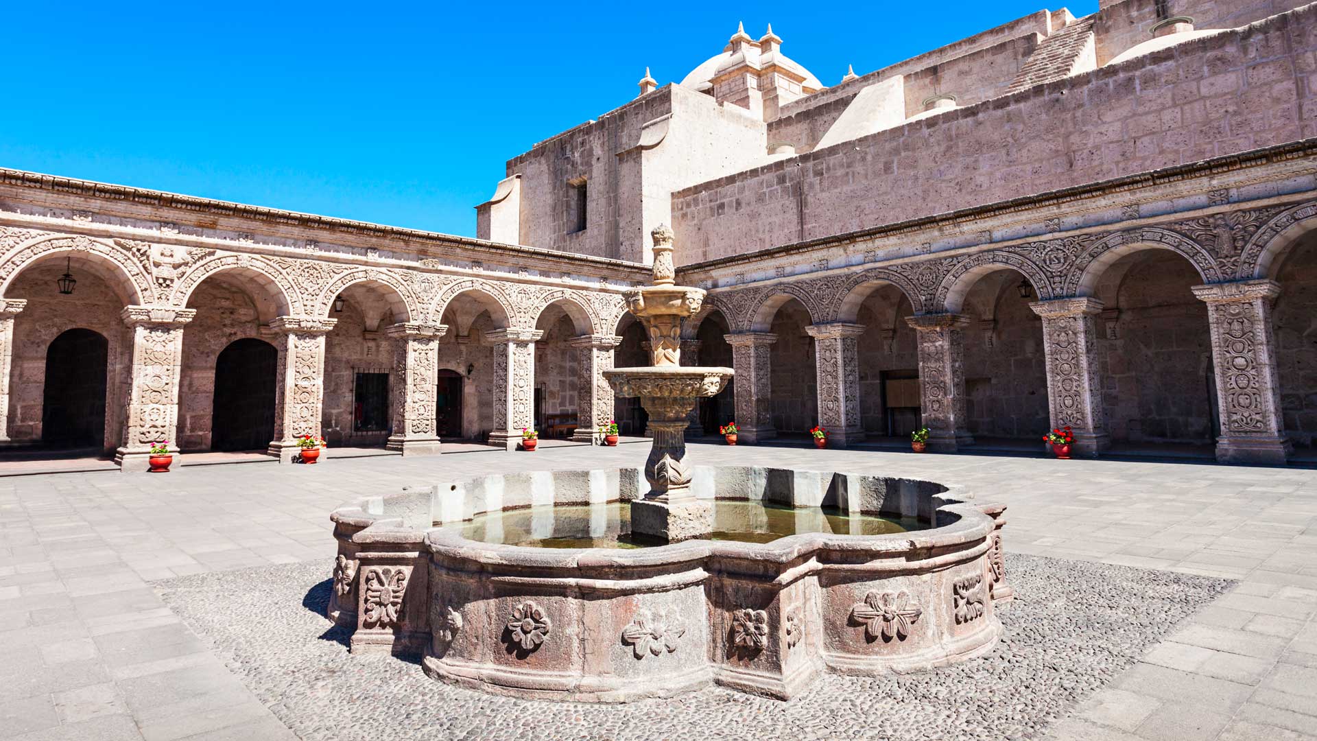 r courtyard of the Iglesia de la Compania in Arequipa, Peru, with sillar stone cloisters and a central fountain under a blue sky.
