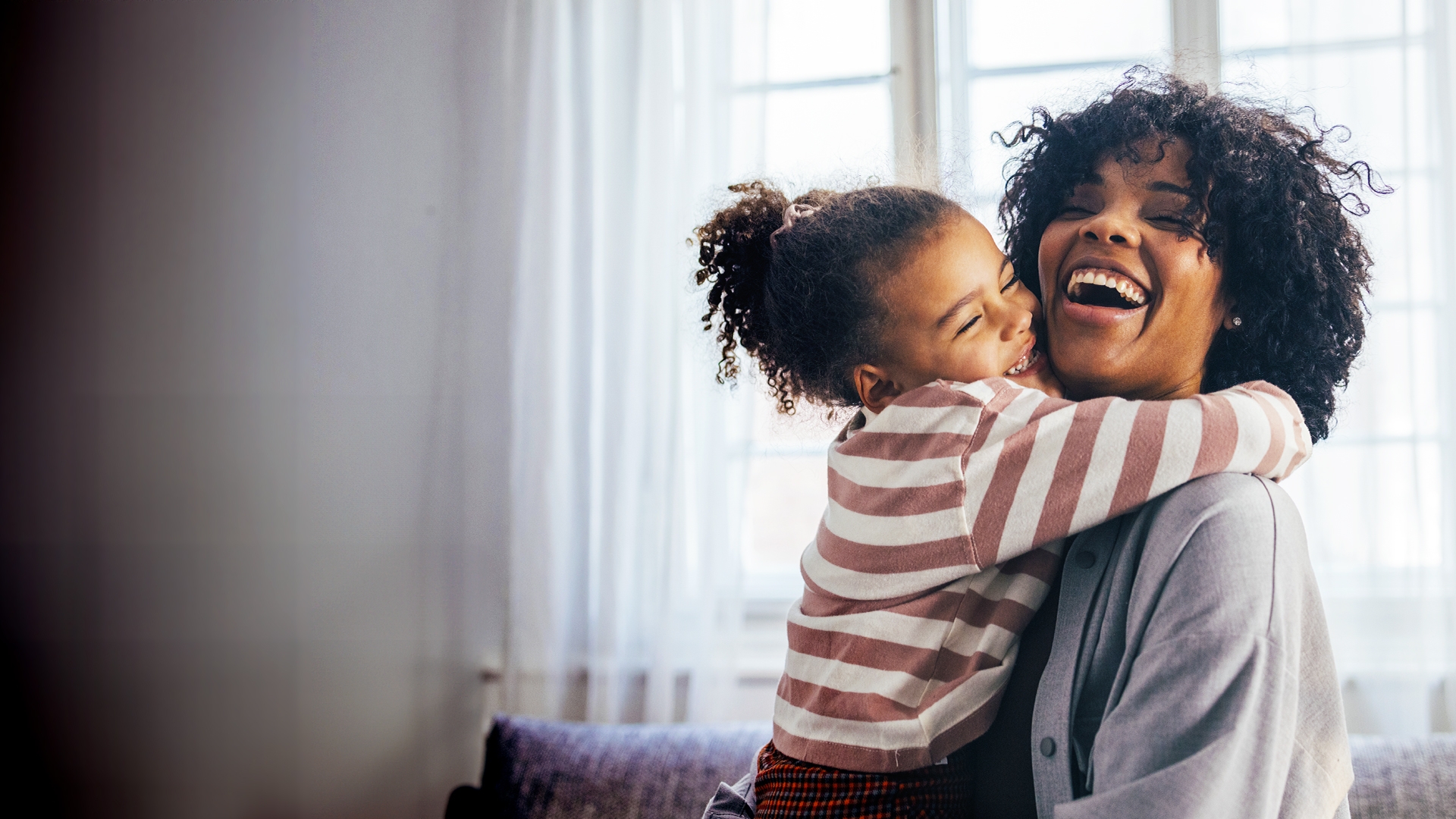 A little girl gives her mother a big hug, who laughs delightedly.