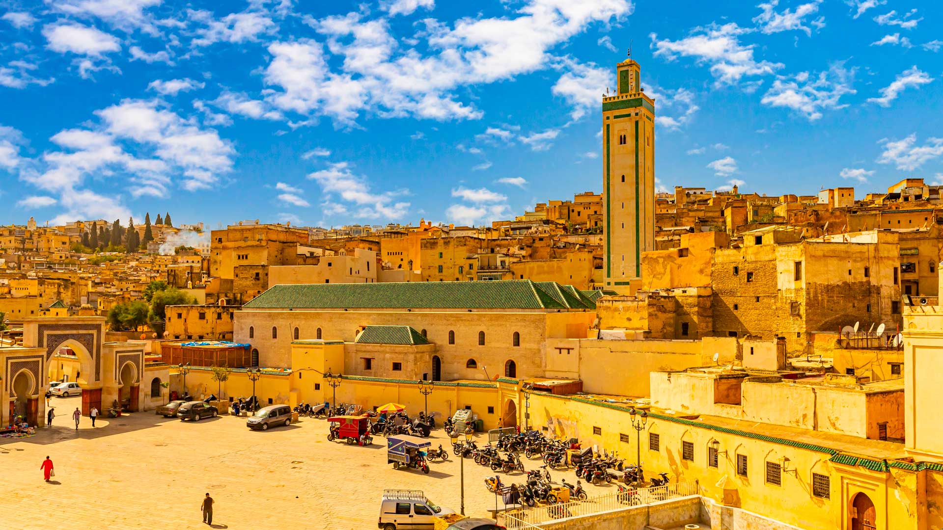 Panoramic view of Fès medina in Morocco, featuring ochre buildings, a mosque, and the Bab Bou Jeloud gate under a blue sky.