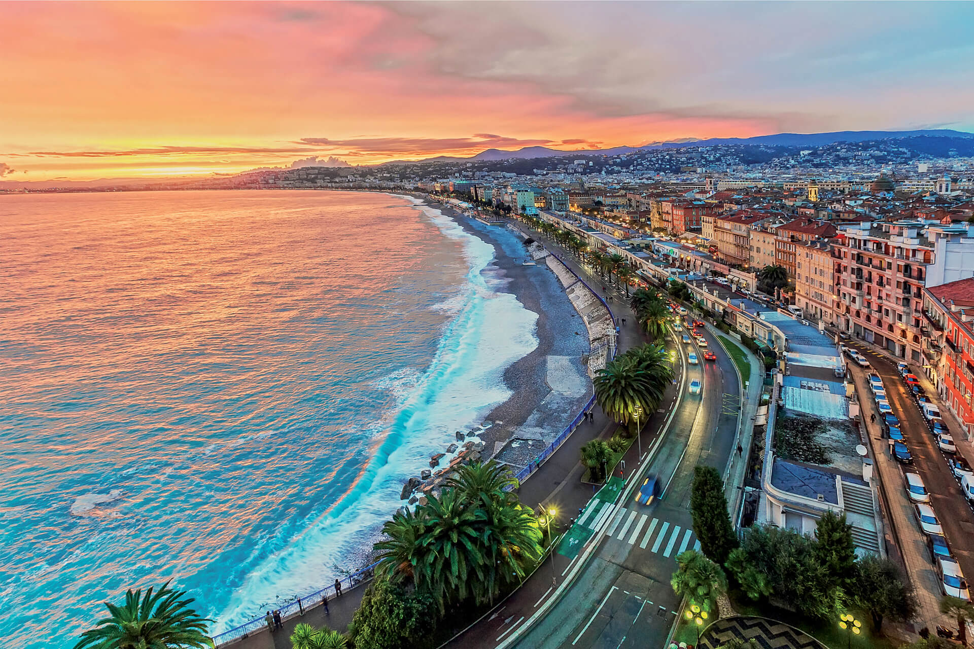 Bird’s-eye view of Nice’s Promenade des Anglais lined with palm trees along the Mediterranean Sea at sunset.