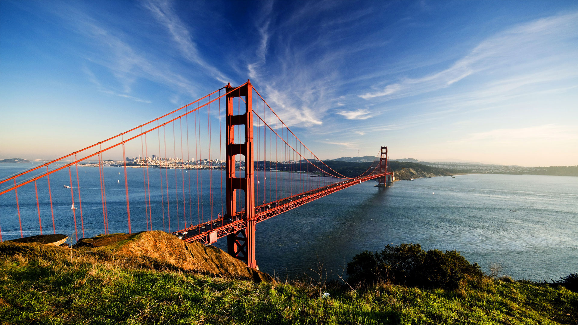 Orange-red Golden Gate Bridge above San Francisco Bay under a blue, partly cloudy sky, California.