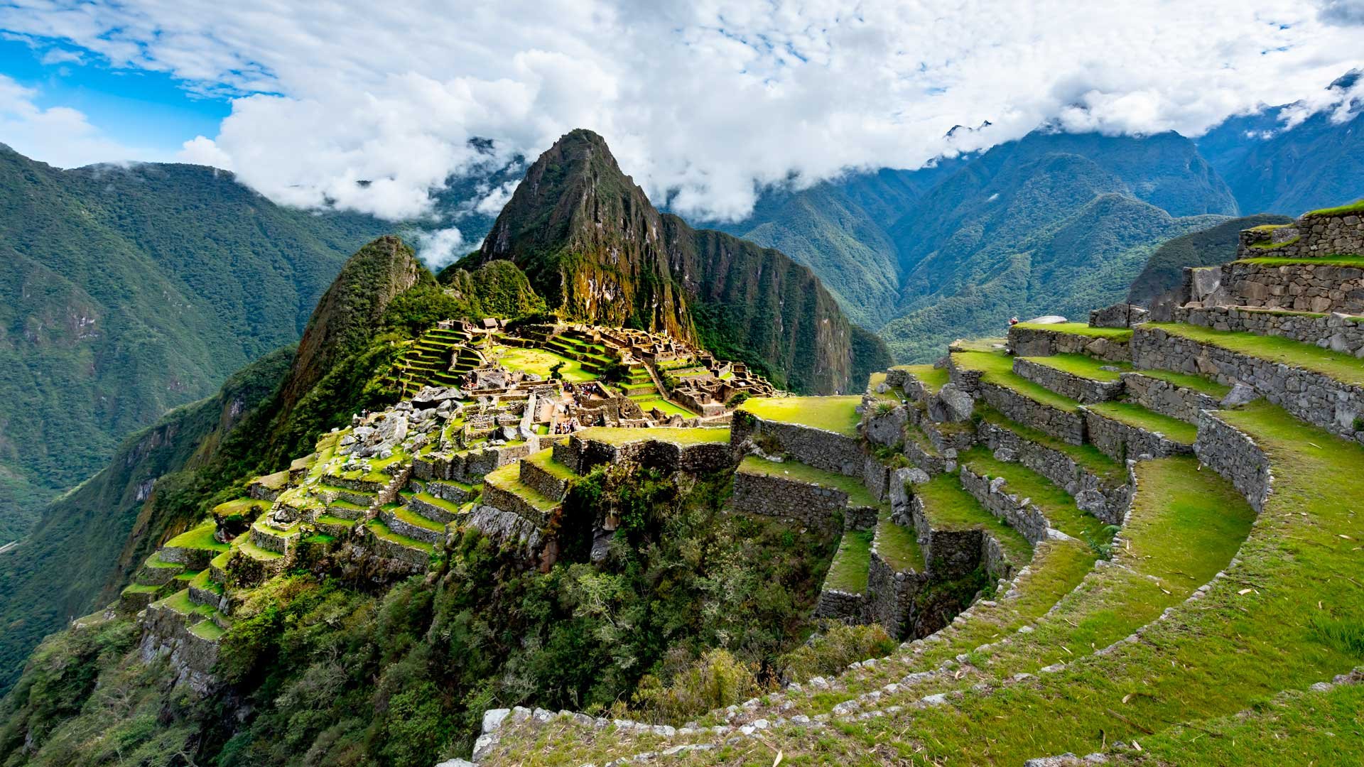 Vue aérienne du Machu Picchu au Pérou, cité inca en terrasses de pierre au cœur de la cordillère des Andes, sous un ciel nuageux. 