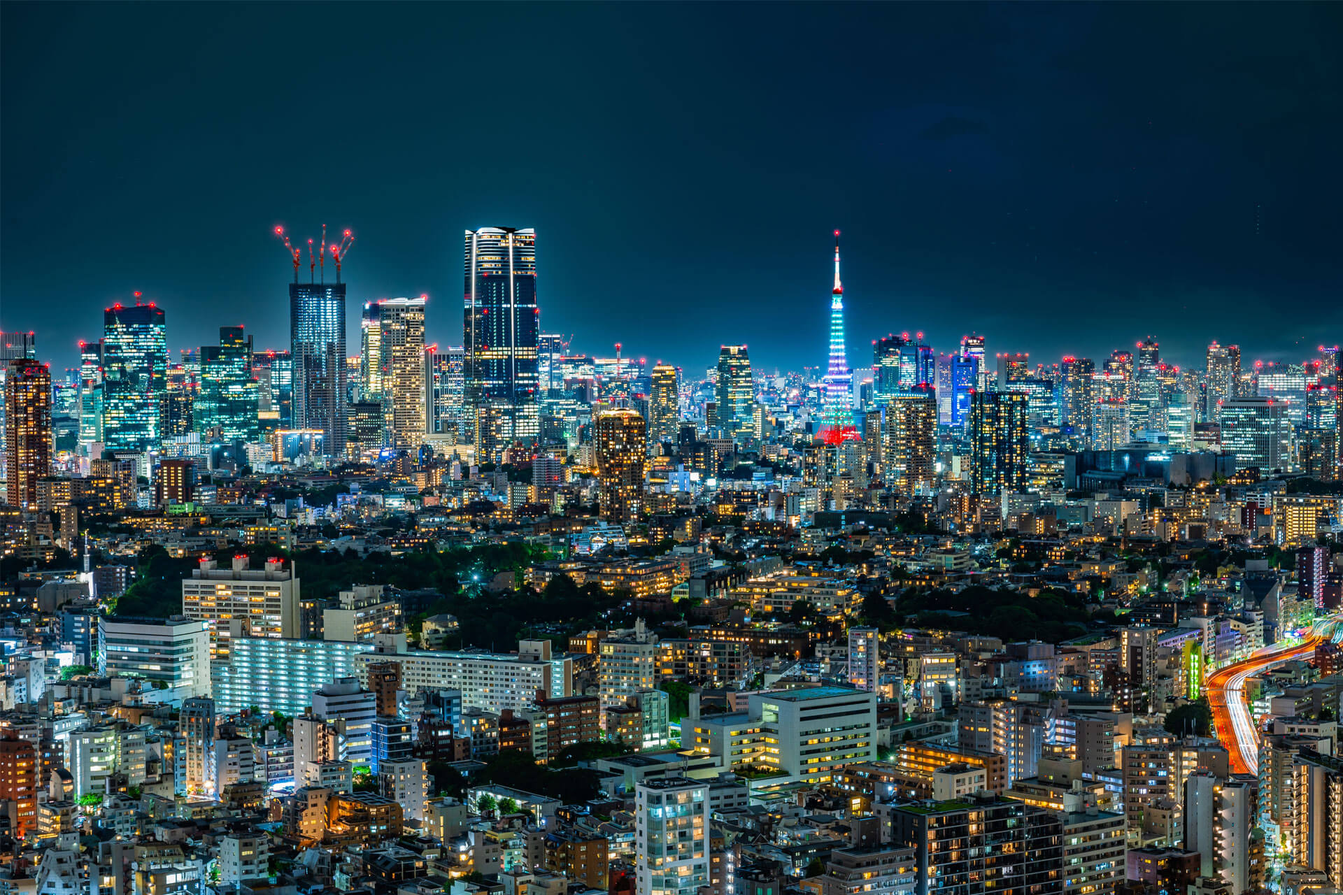 Aerial night view of downtown Tokyo, Japan, with illuminated skyscrapers and the Tokyo Tower glowing in blue and red.