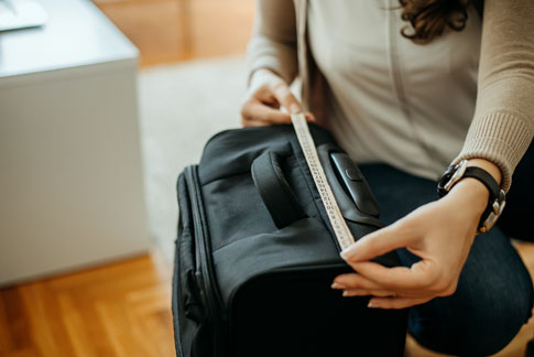 Agenouillée près d’une valise de cabine, une femme la mesure pour être conforme avec la compagnie aérienne.