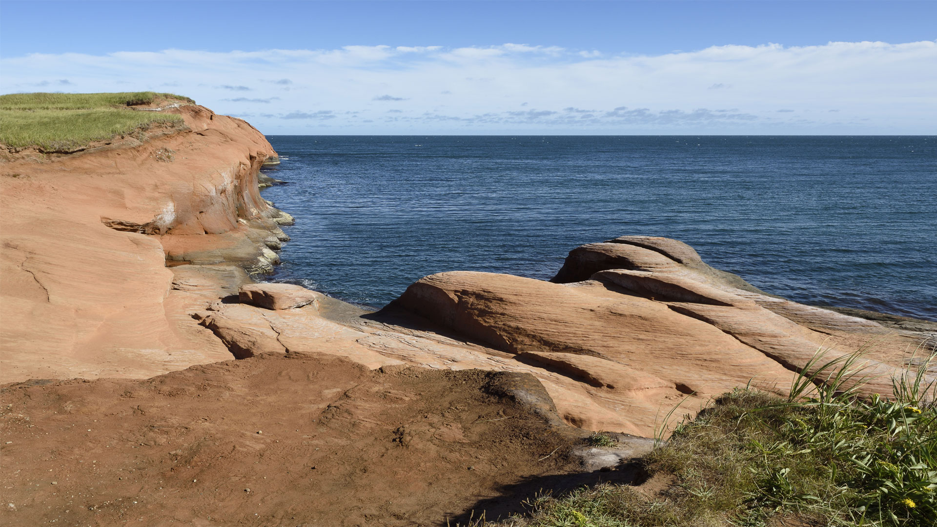 Red sandstone cliffs with coastal vegetation and blue sky in Grande-Entrée, Magdalen Islands.