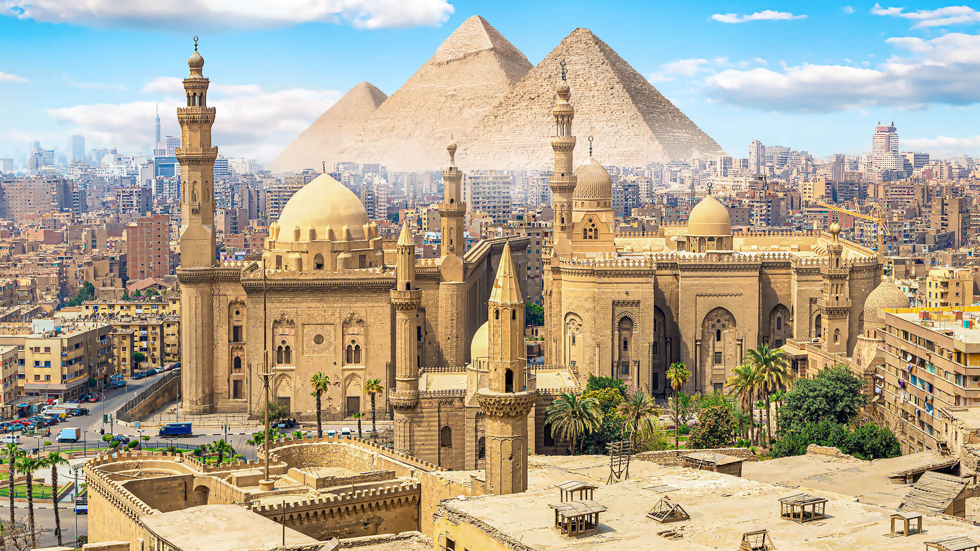 Cairo with historic mosques in the foreground and the Giza Pyramids towering on the horizon under a blue sky.