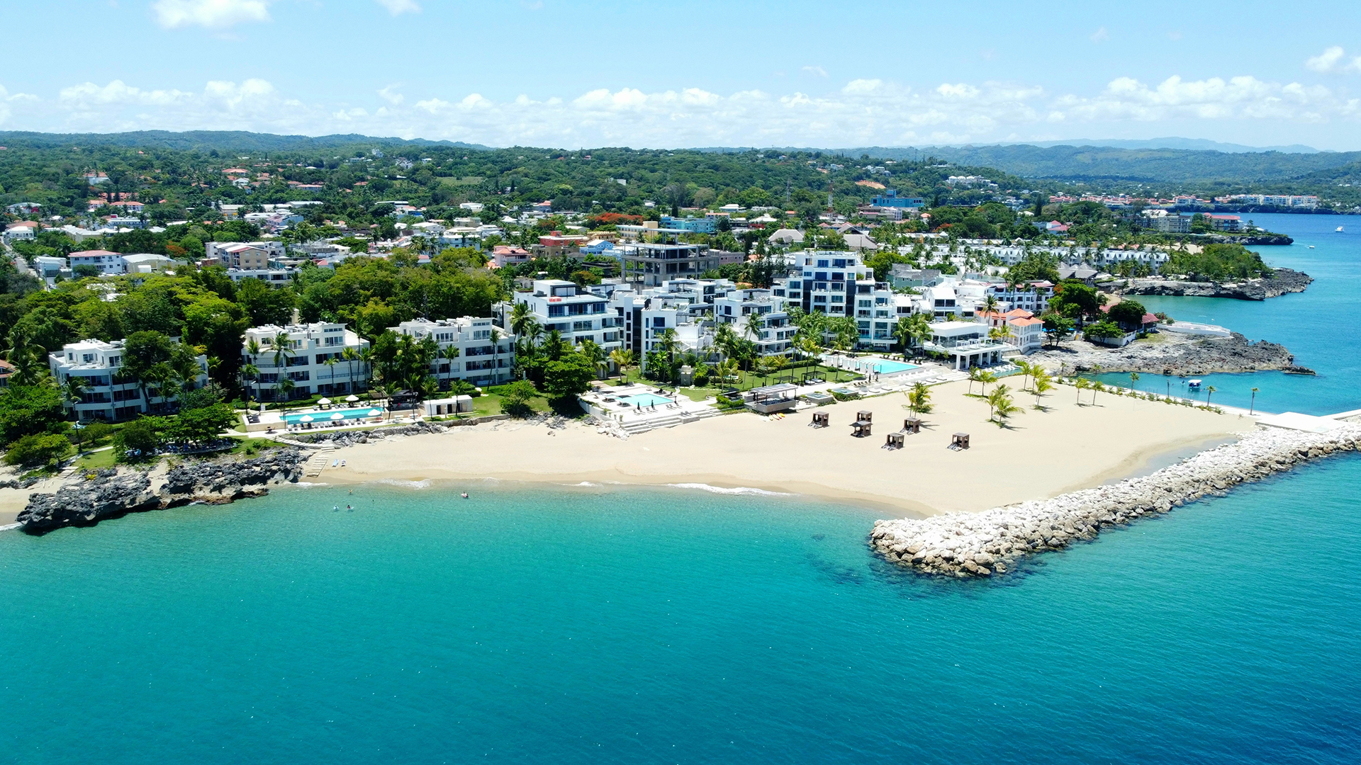 Aerial view of Sosúa, Dominican Republic, featuring a white-sand beach, modern buildings, and turquoise waters.