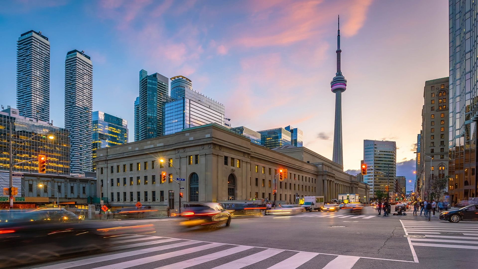 Panoramic view of Toronto, Ontario, featuring the CN Tower, modern skyscrapers, Union Station, and busy traffic at dusk.