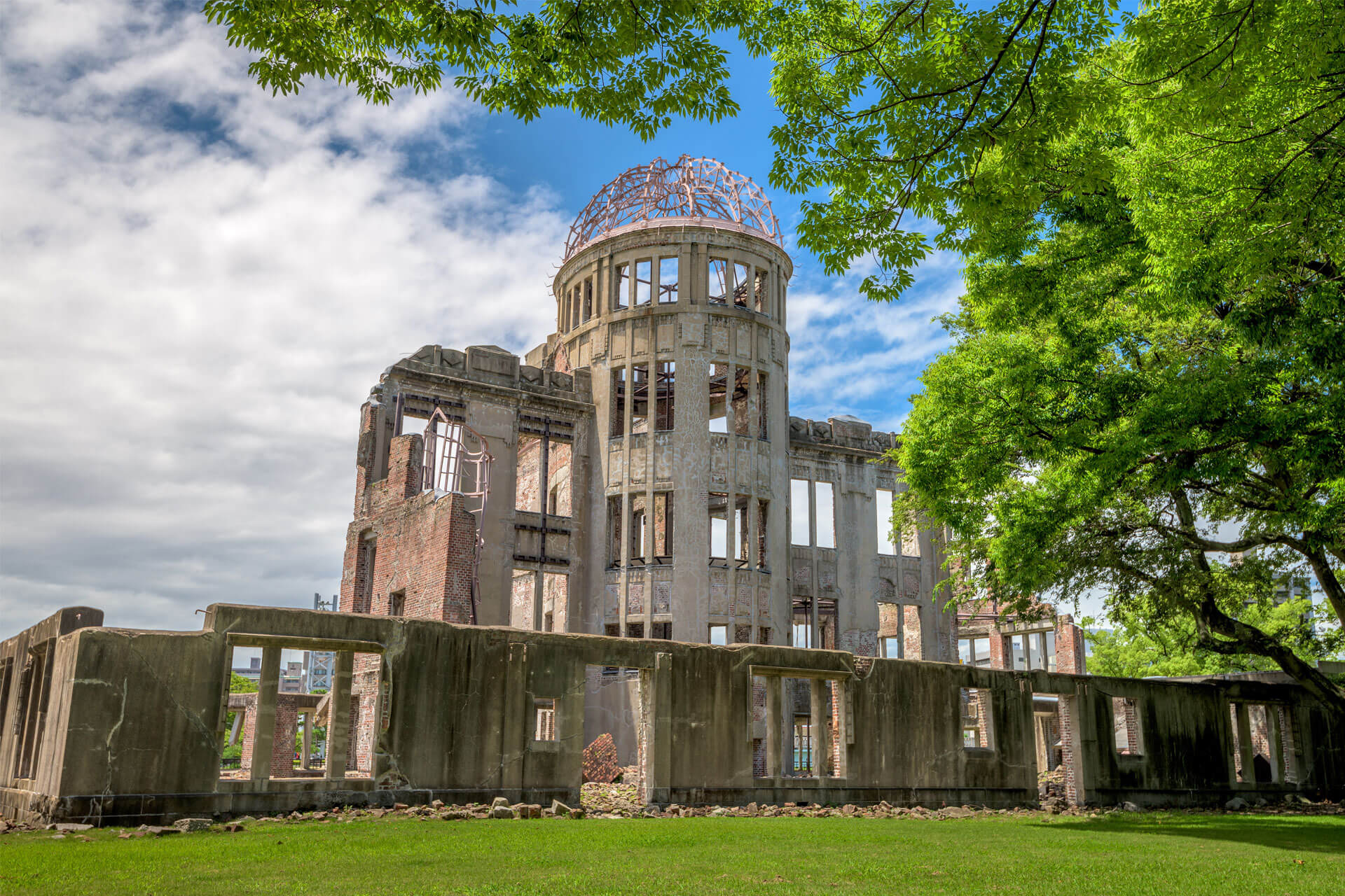 Ruins of the Genbaku Dome in Hiroshima Peace Memorial Park, Japan, surrounded by lush green trees.