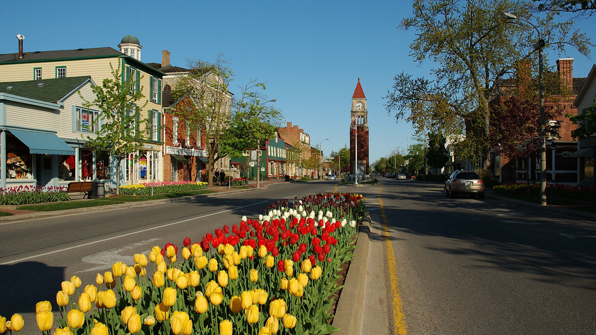 Queen Street in Niagara-on-the-Lake lined with colourful historic buildings and tulips, with a clock tower in the distance.