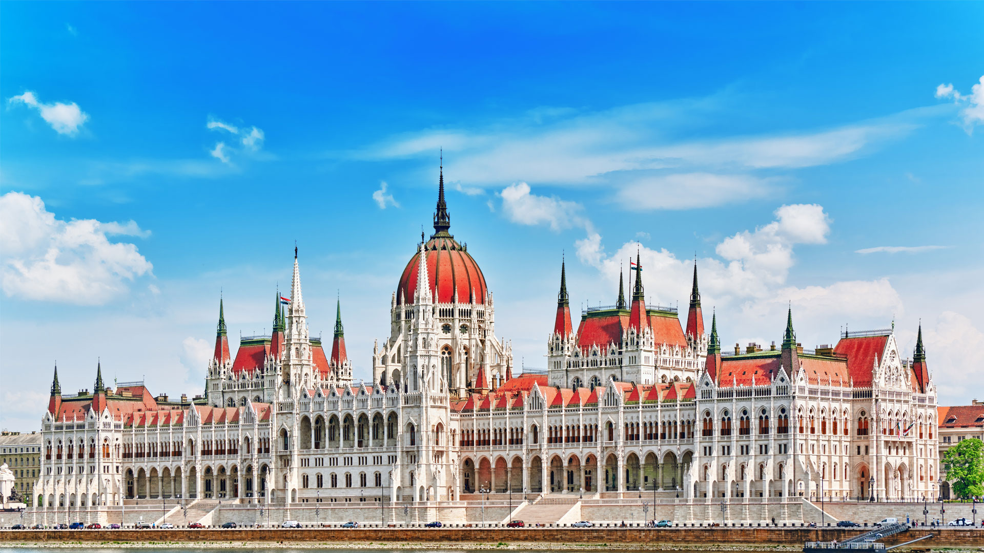 Parlement de Budapest vu depuis le Danube de jour, avec son architecture blanche majestueuse et son toit orangé emblématique.