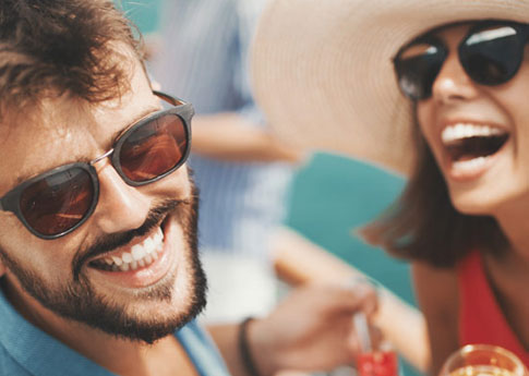 Sur le pont d’un navire de croisière, un couple tout sourire prend l’apéro.