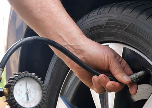 Close-up of hands holding a pressure gauge and measuring tire pressure.