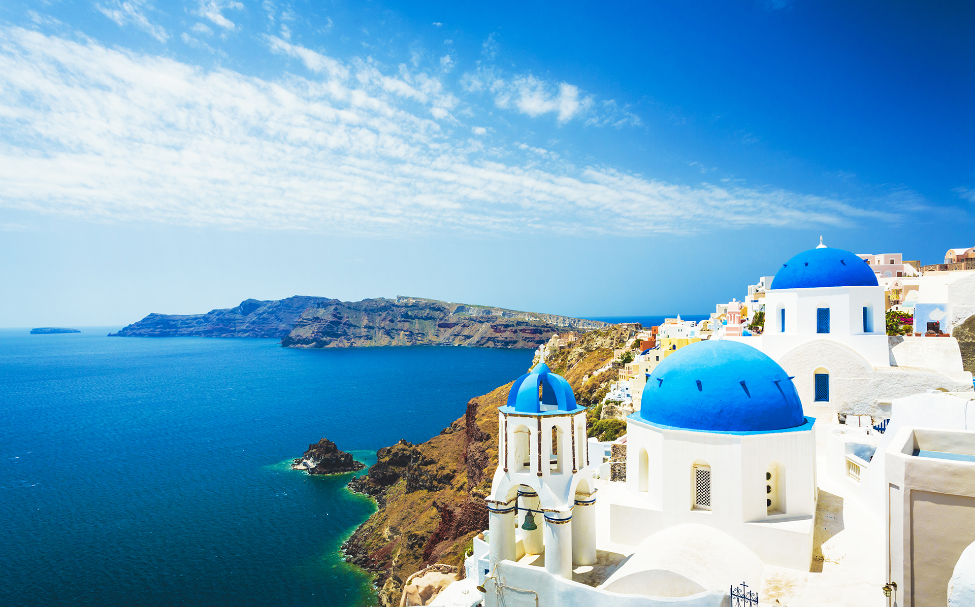 Vue panoramique des maisons blanches aux dômes bleus de Santorin, en Grèce, avec la mer Égée, sous un ciel ensoleillé.