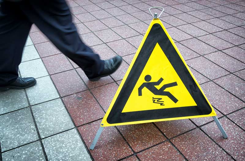 Public sidewalk with a yield sign displaying a cartoon of someone slipping