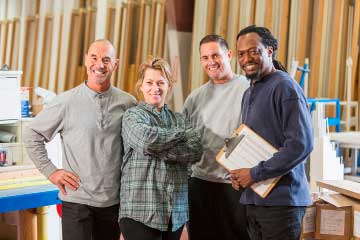 Three men and a woman smiling in a warehouse. One man is holding a clipboard.