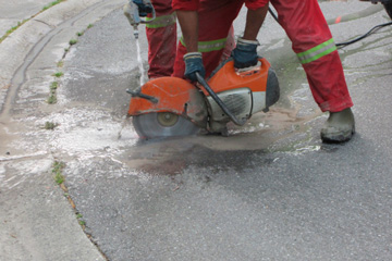 Worker in orange jumpsuit cutting concrete and using the wet method of protection from silica.