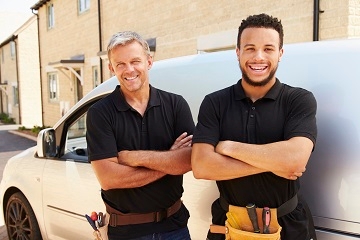 An older white man and a younger African American man smile in front of a white delivery truck