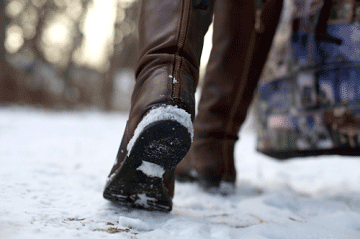 Close up of someone's boots as they walk on an icy sidewalk