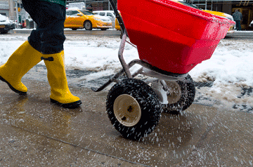 Someone using a salt sprayer to melt ice on a sidewalk