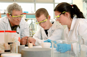 Two students and a teacher in lab equipment assessing a sample