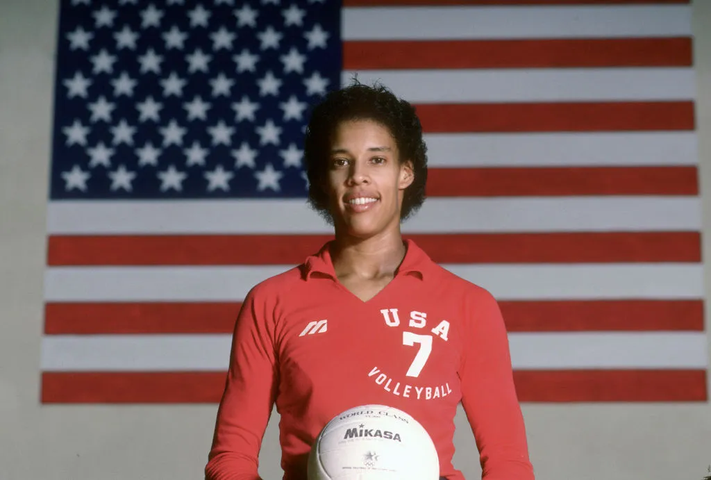 Olympian Flo Hyman standing with a volleyball in front of the American flag.