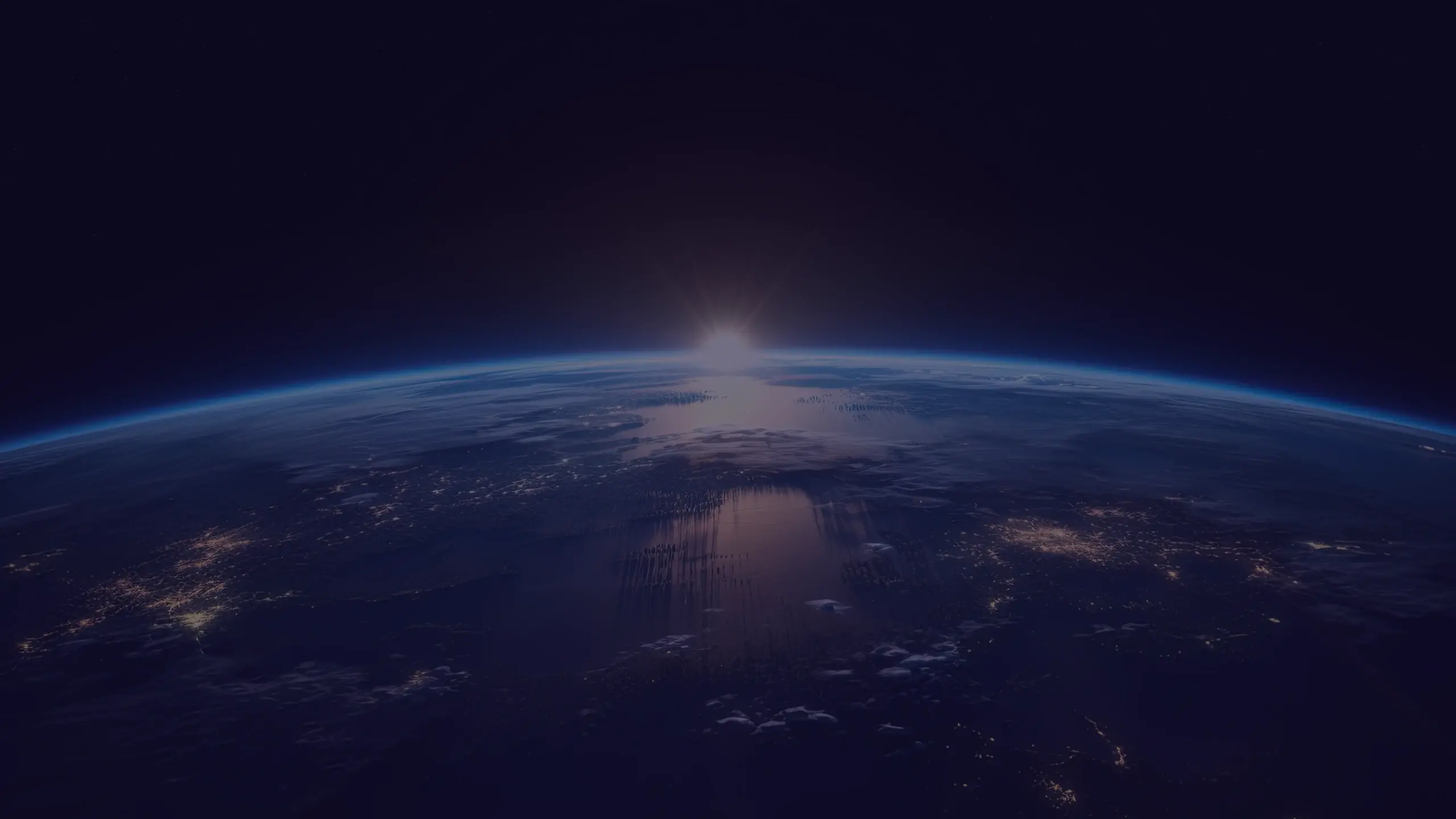 Earth at sunrise from space, with a bright sun glow and reflected light across the dark blue clouded horizon
