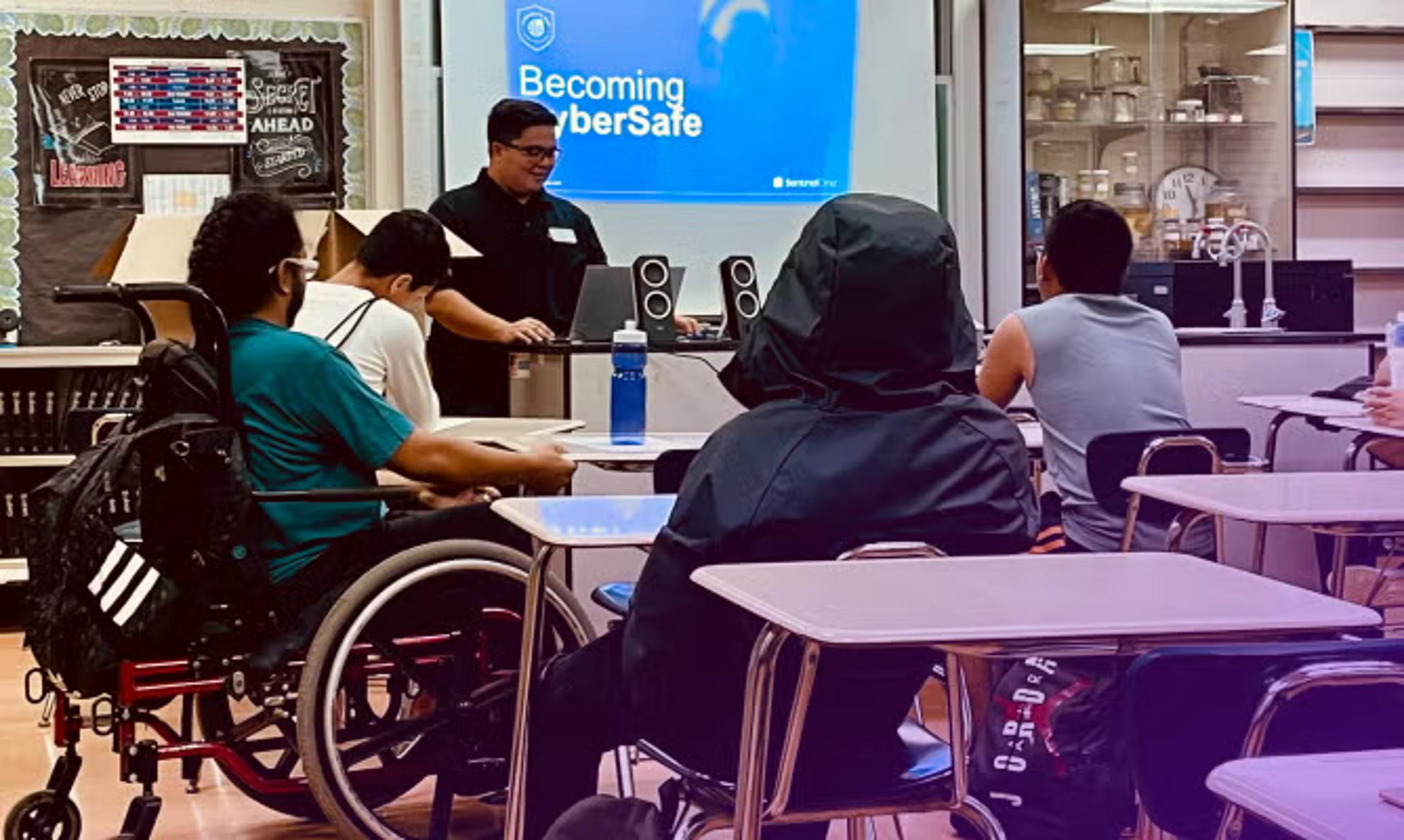 Training classroom with people seated facing instructor; front screen says “Becoming CyberSafe” and wall sign says “AHEAD”