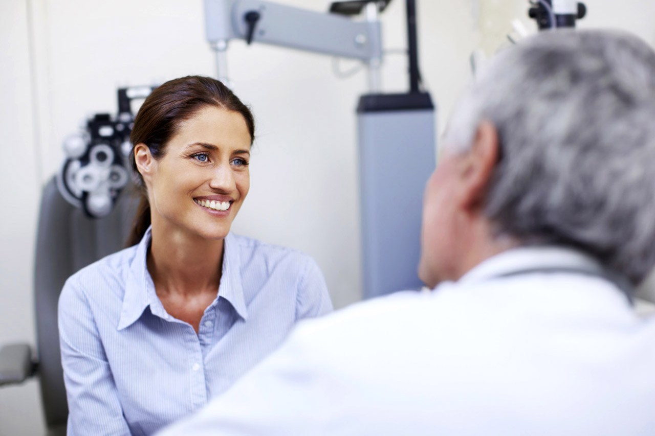 Smiling young woman being attended to by a doctor. Doctor attending to a young patient in his eye clinic.