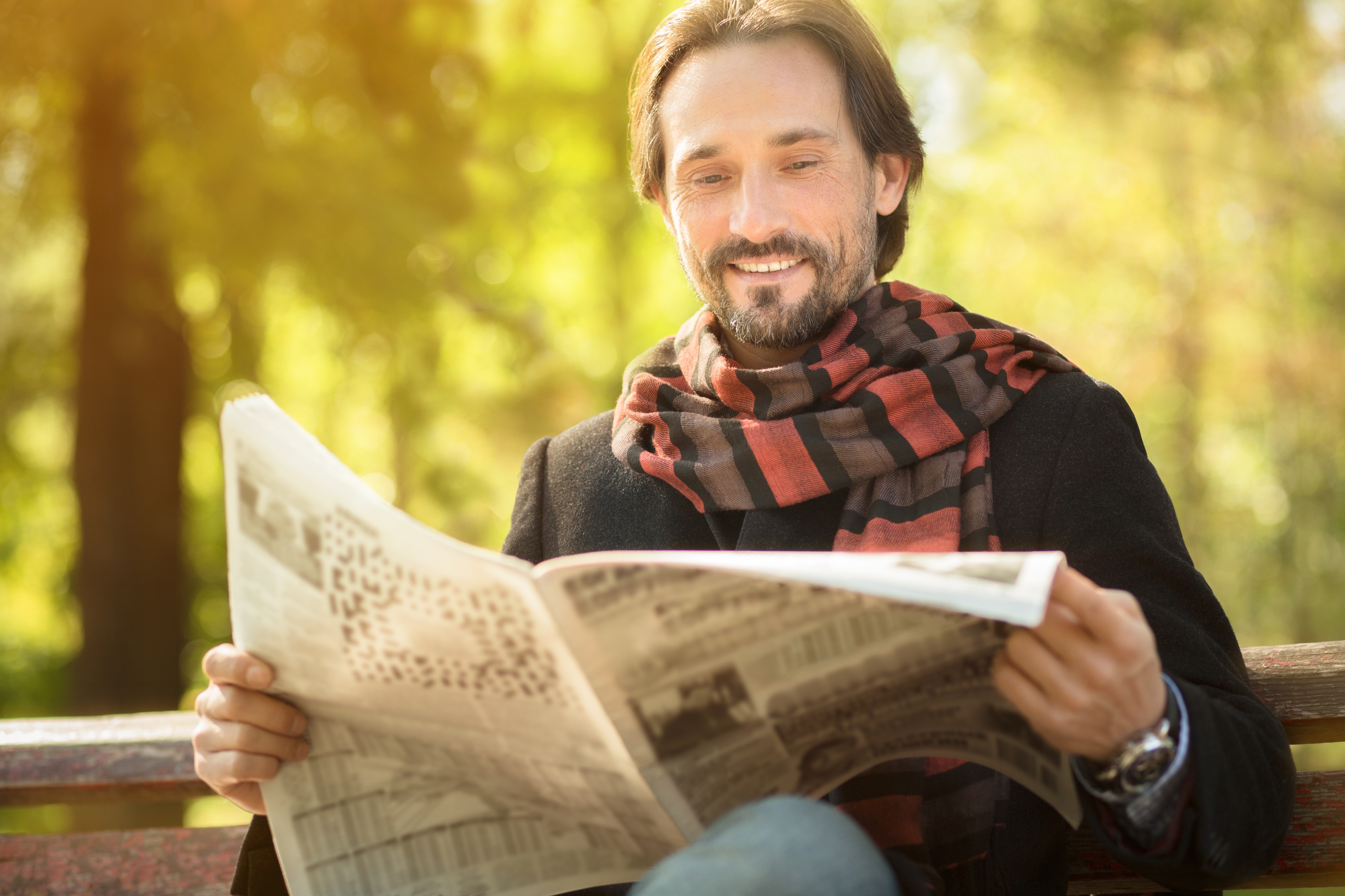 Een man die een krant leest op een bankje in het bos met een sjaal om