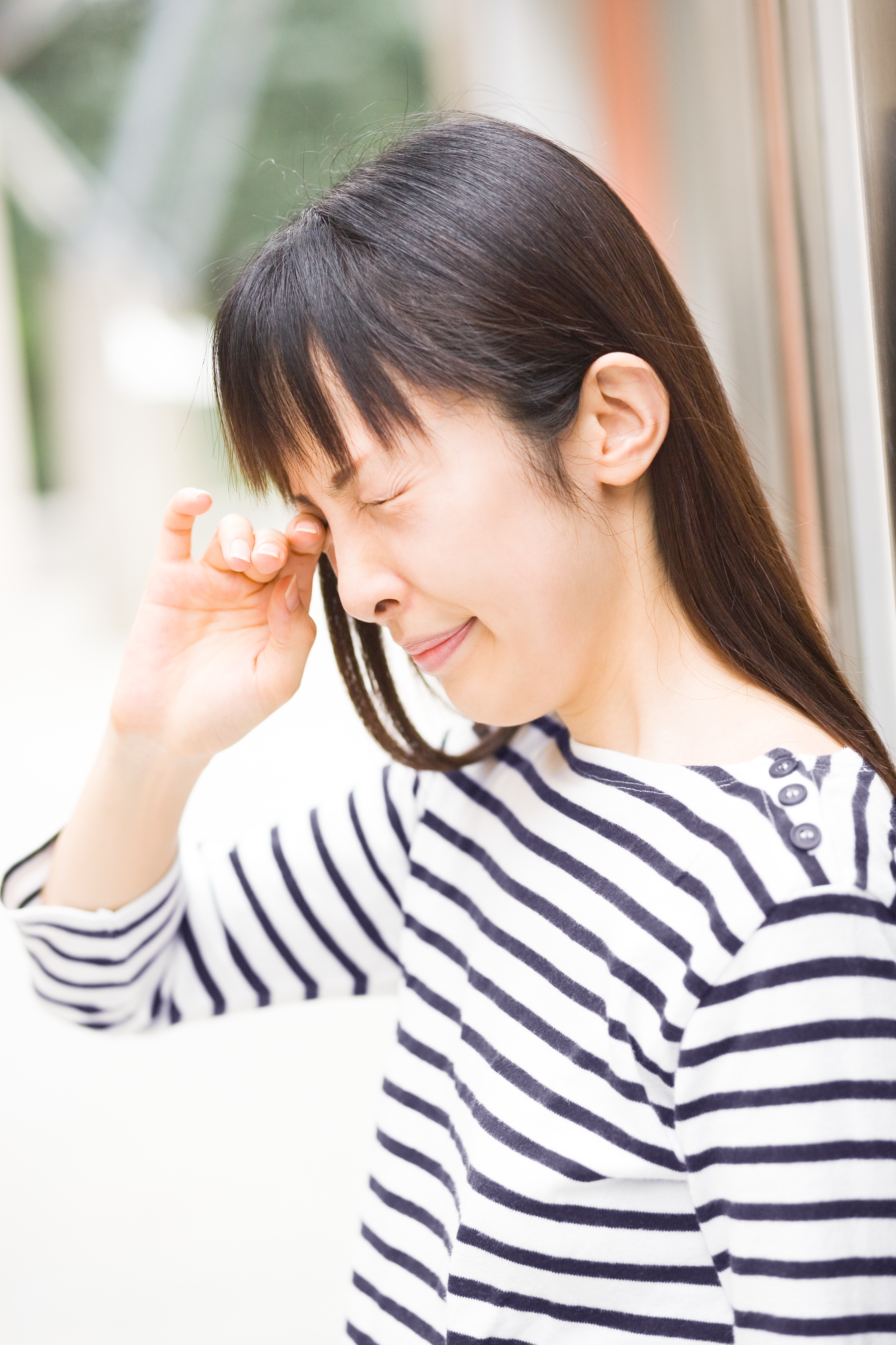 A woman with black & white strip rubbing her eye at the park