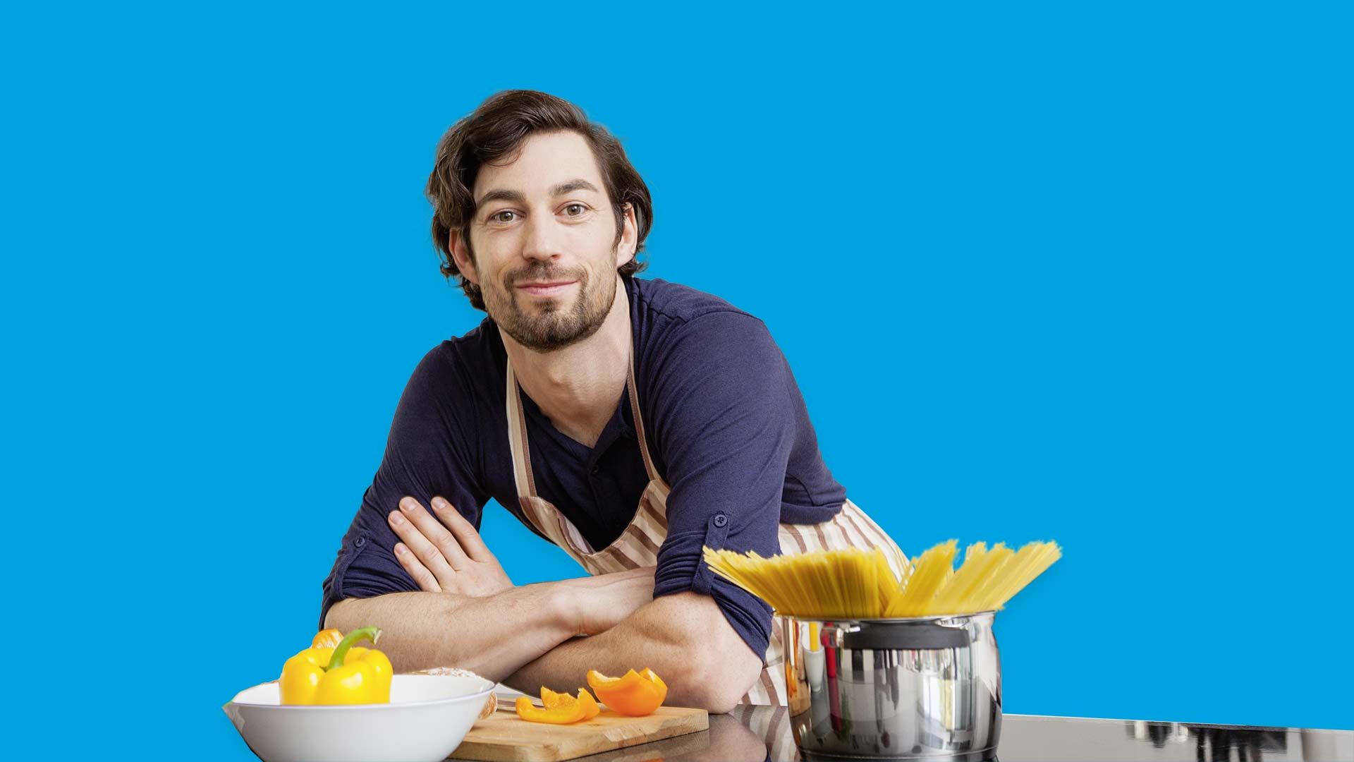 Young man with a beard leaning on a kitchen counter, about to start cooking pasta.